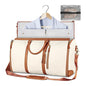 Beige foldable travel bag  with brown straps, shirt on hanger, and clear pouch on white background
