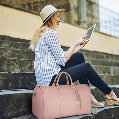 Woman sitting on steps using a tablet with a pink duffel bag beside her